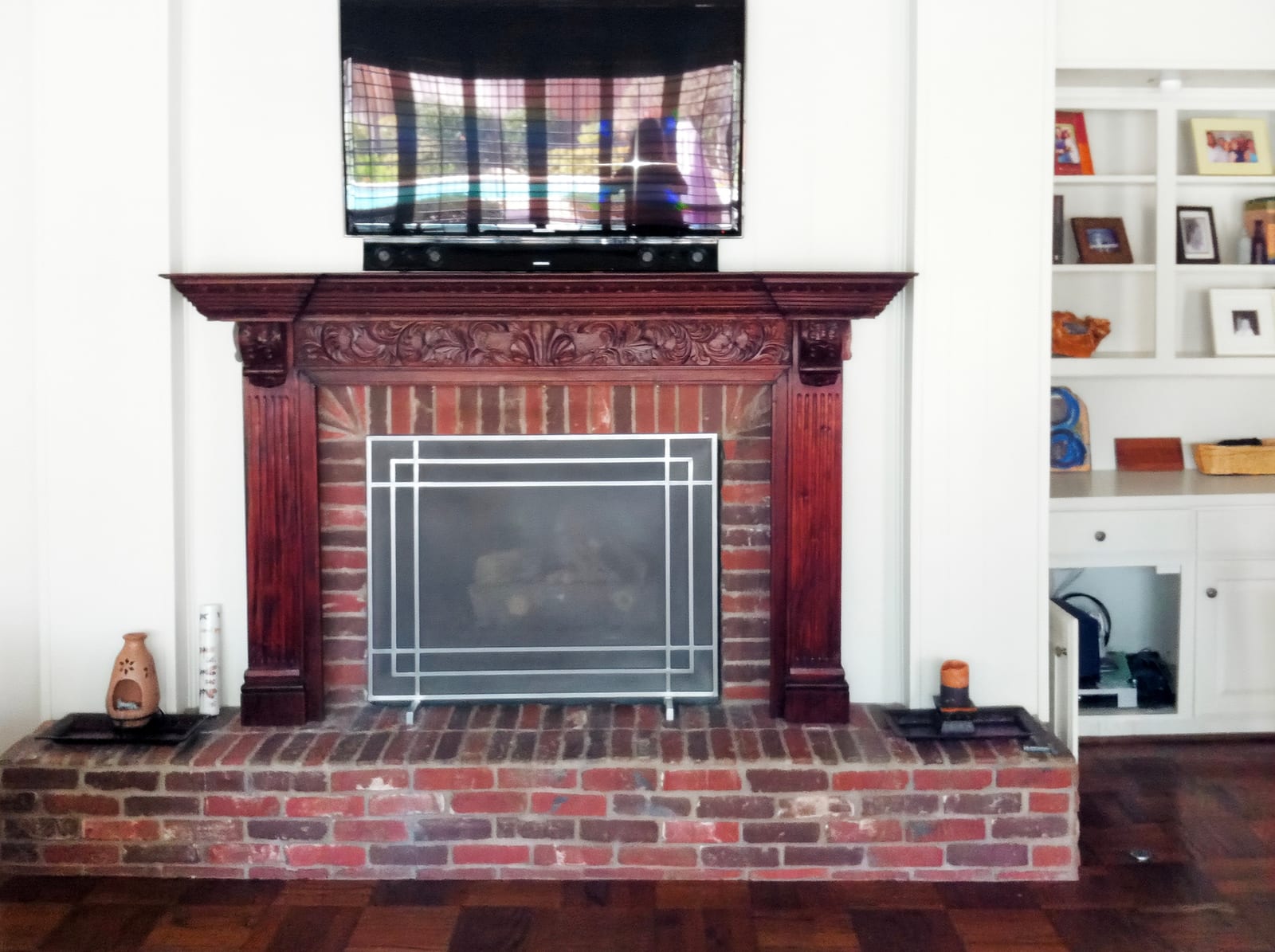 Red brick fireplace with a heavy dark wood mantel and a television above