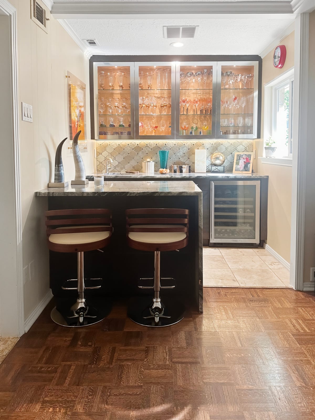 Wet bar with a lighted glass-front cabinet, black counter and bar stools