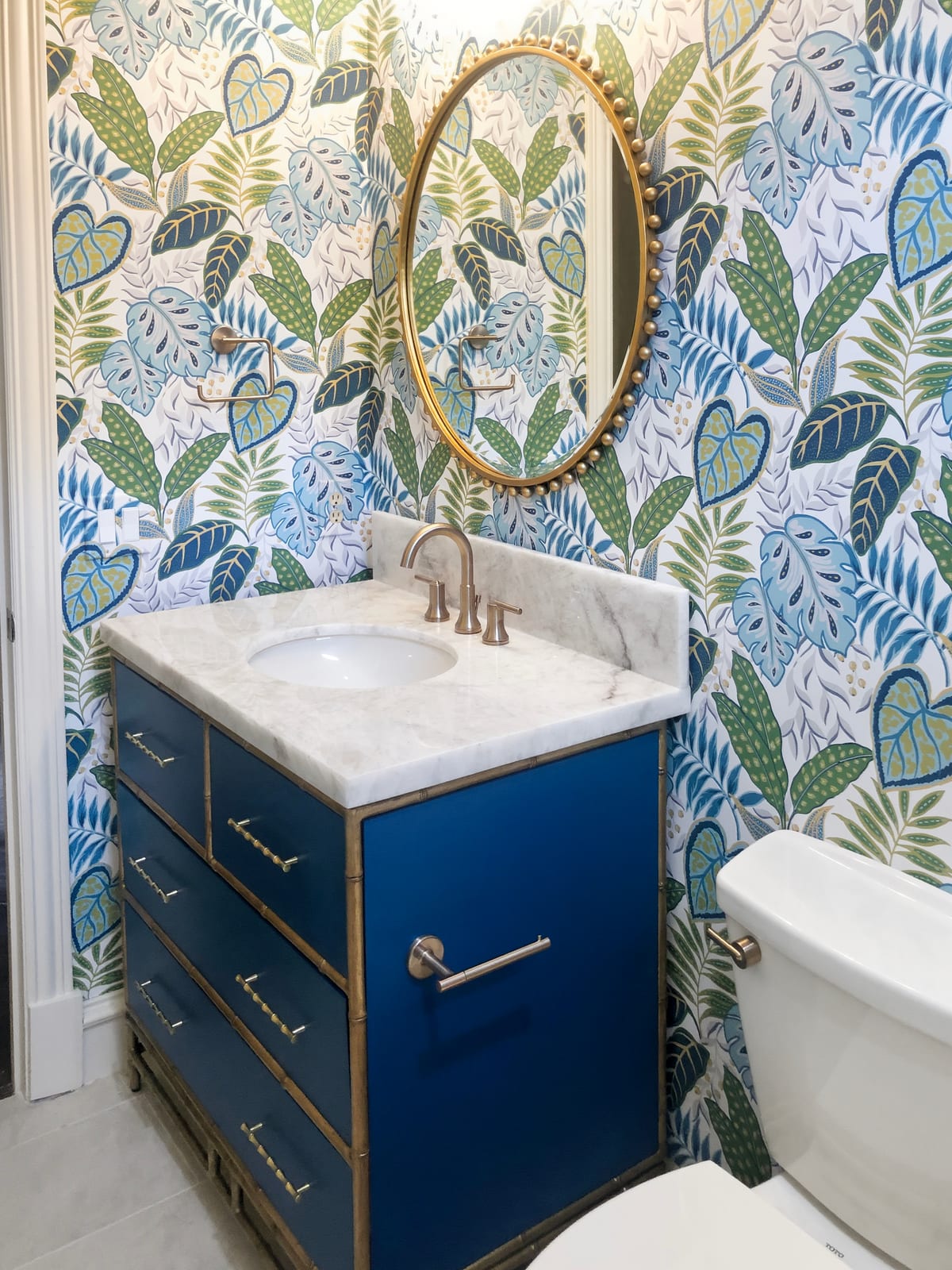 Guest bathroom with botanical wallpaper, a navy vanity and a brass mirror