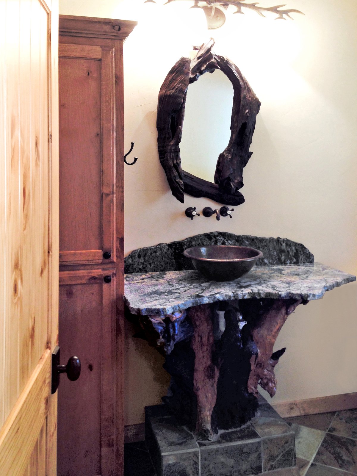 Rustic powder room with a stone vessel sink on a driftwood base and antler sconce