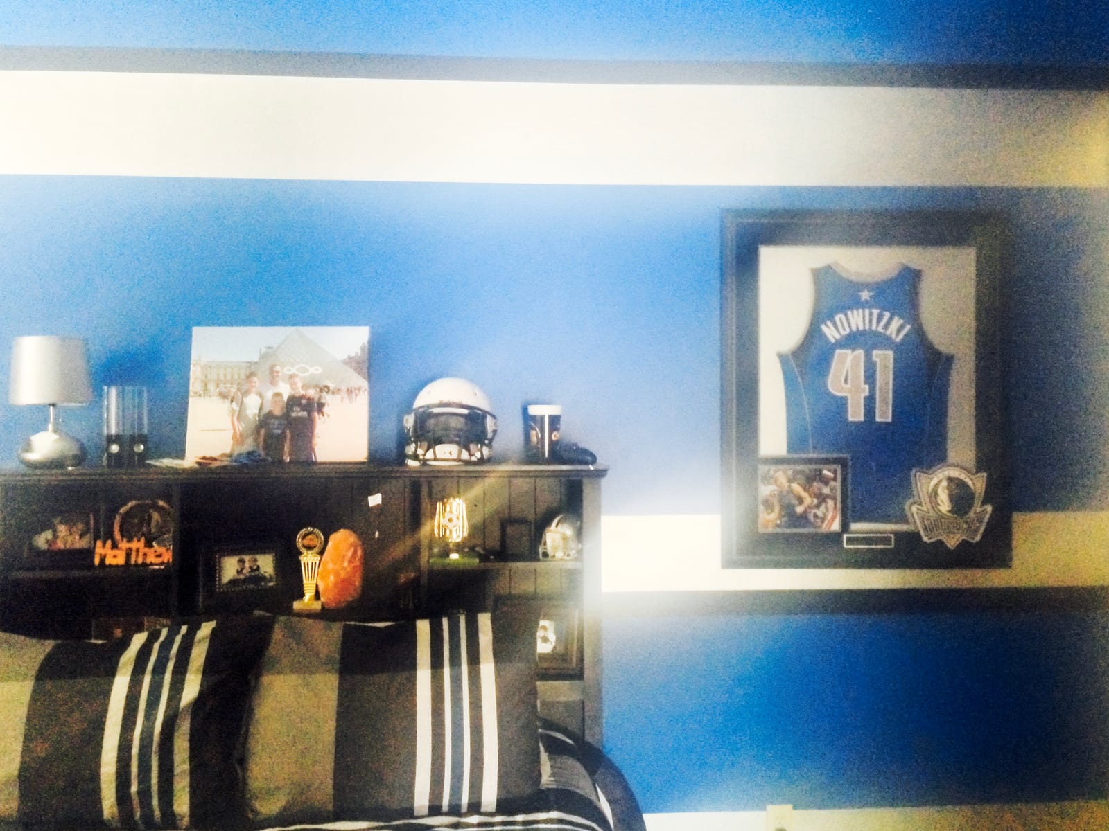 Bedroom with a blue and white striped wall, bookcase headboard and framed jersey