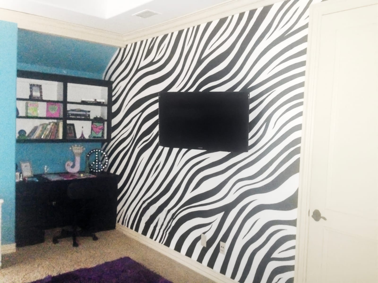 Bedroom with a zebra accent wall, teal walls and a wall-mounted television