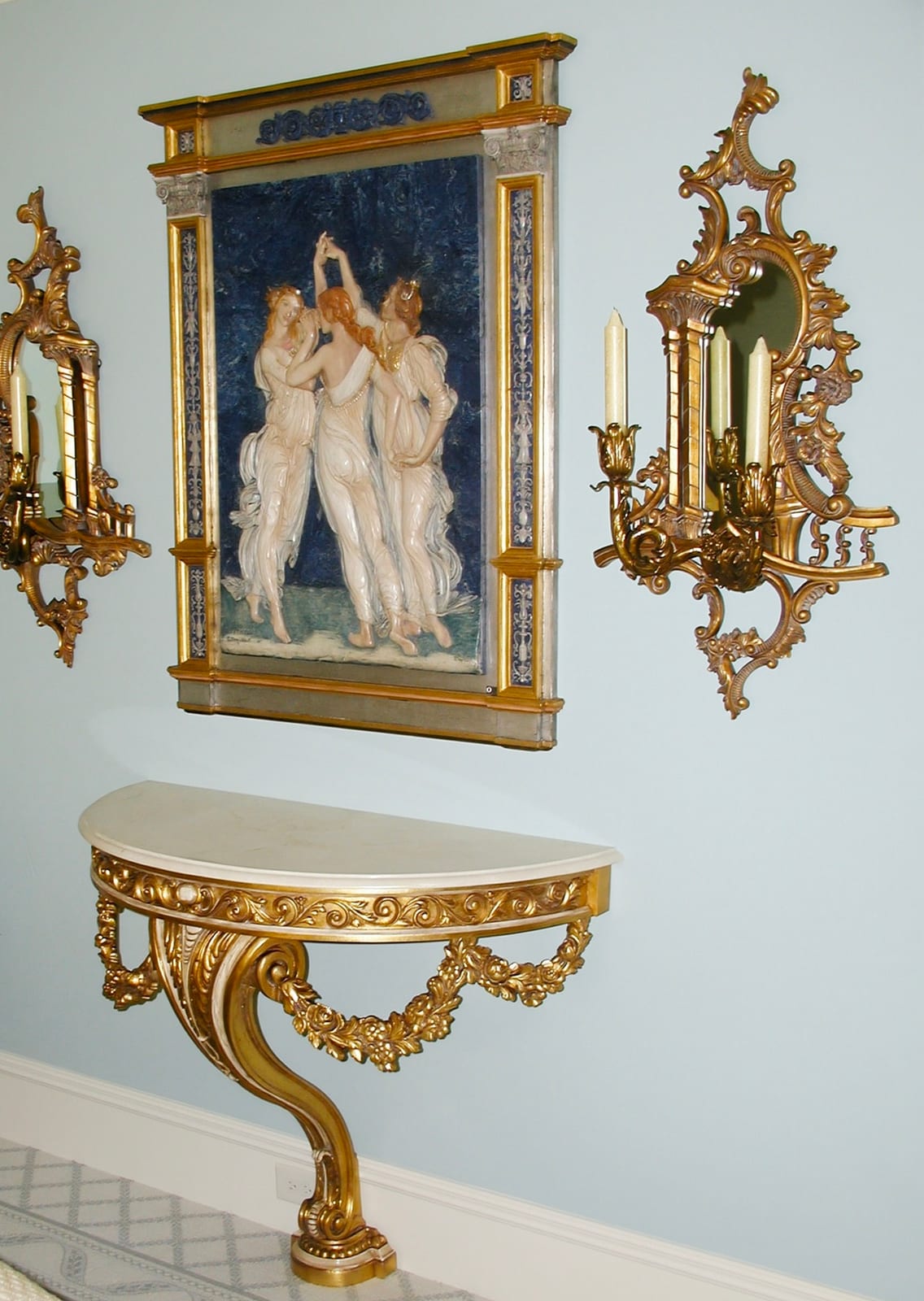 Gilded console beneath a classical painting with sconces