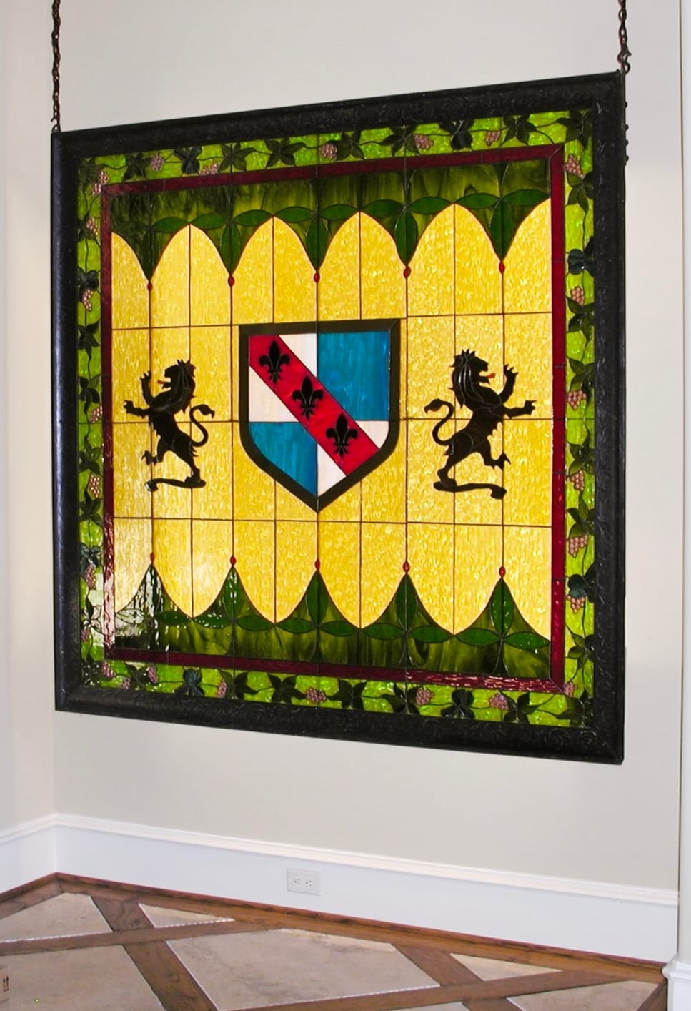 Heraldic stained glass panel with lions and a shield, designed by Jan Revels and hung in a window