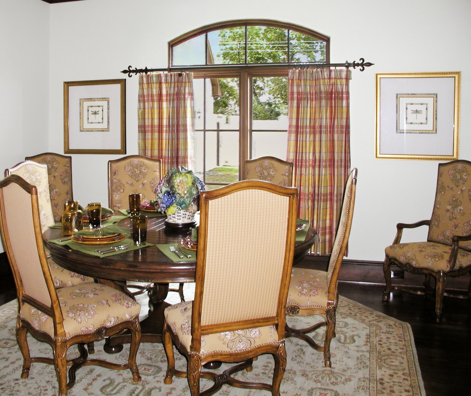 Round dining table with plaid drapes, tapestry chairs and a glass centerpiece