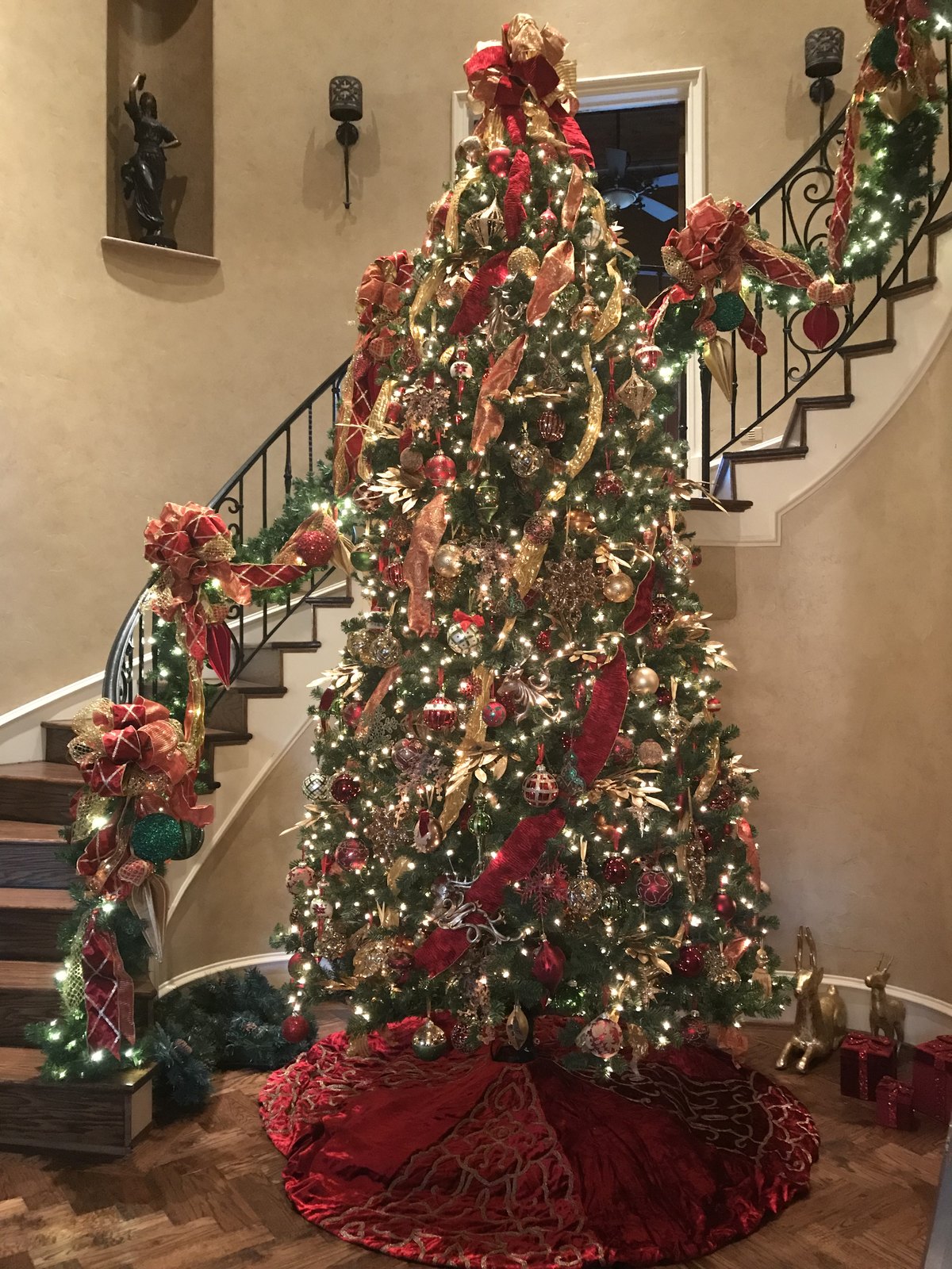 Full Christmas tree decorated in red and gold ribbon beside a curved staircase