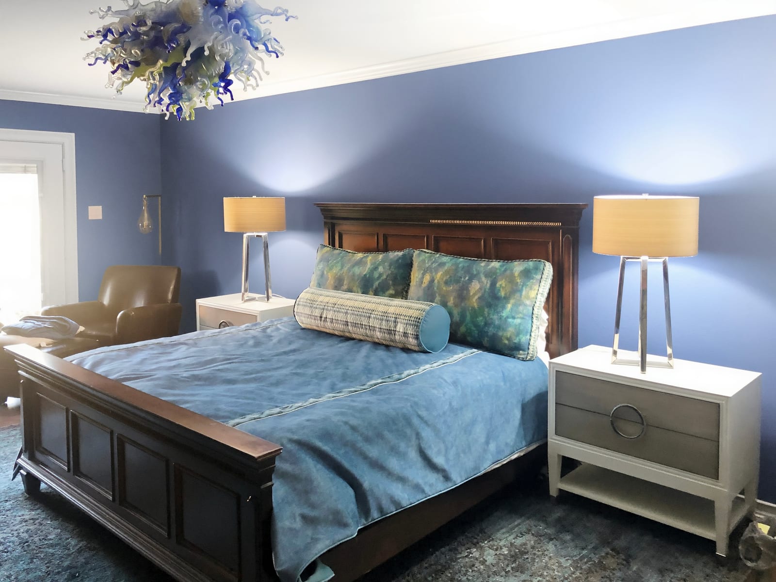 Master bedroom in blue with a carved wood bed and a blown-glass chandelier