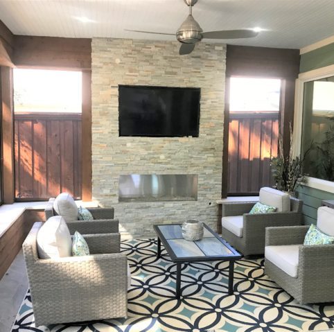 Covered outdoor lounge with a stone fireplace, patterned rug and cushioned seating
