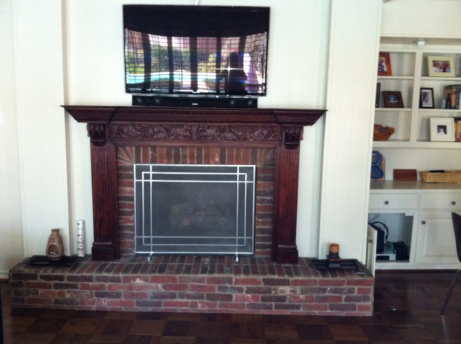 Red brick fireplace with a heavy dark wood mantel and a television above
