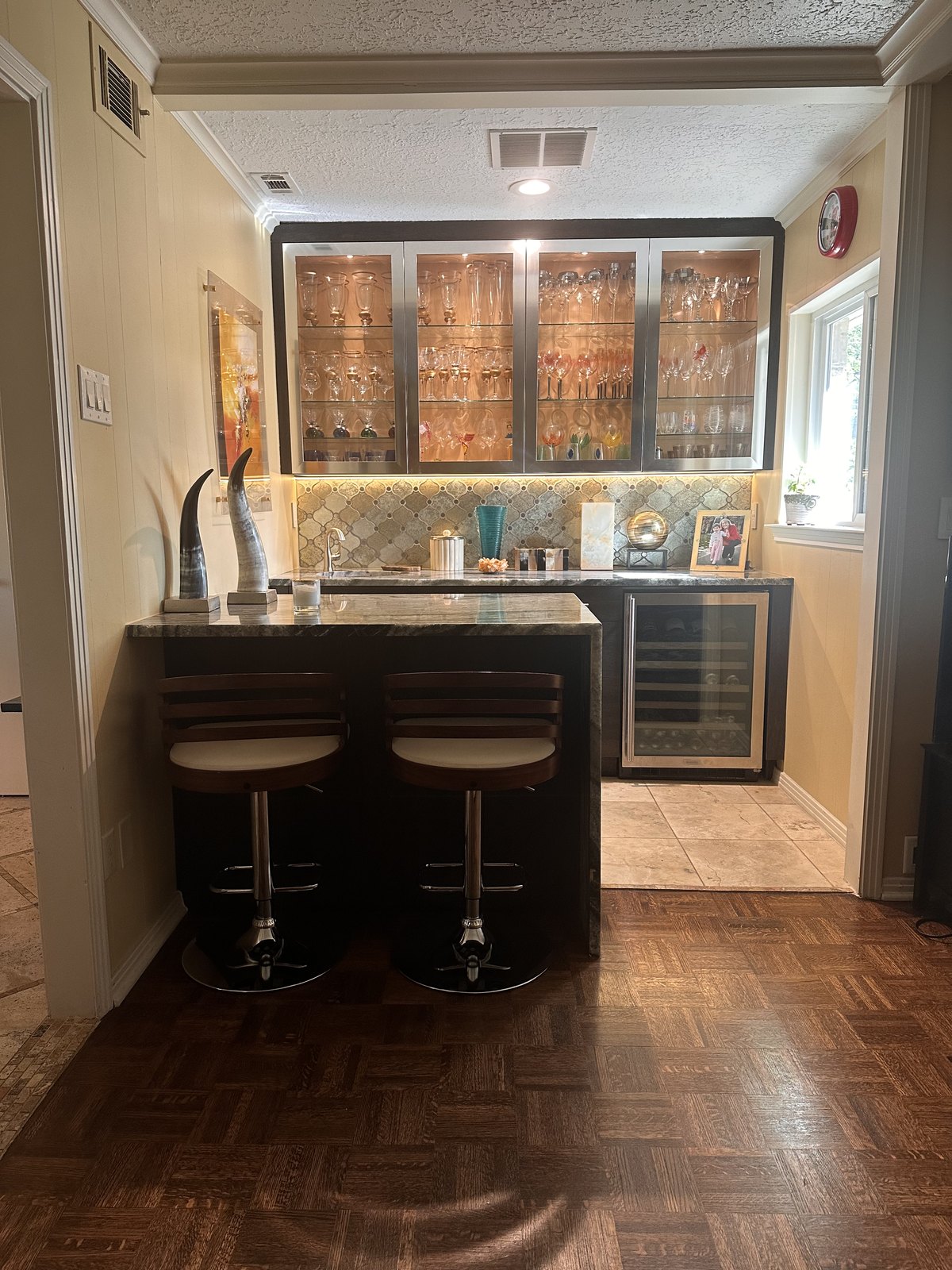 Wet bar with a lighted glass-front cabinet, black counter and bar stools