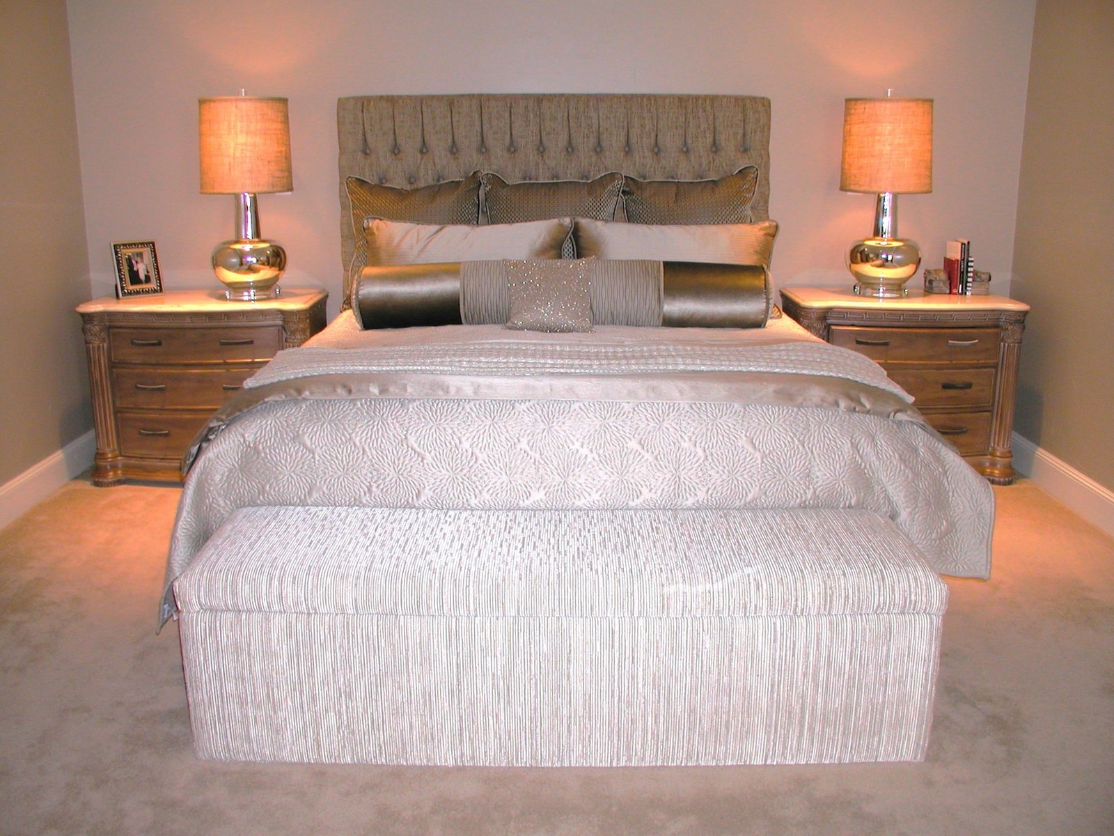 Master bedroom with a tufted headboard, carved wood nightstands and warm lamplight