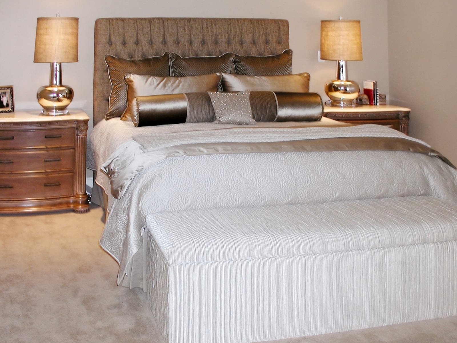 Master bedroom with a tufted headboard, carved wood nightstands and warm lamplight