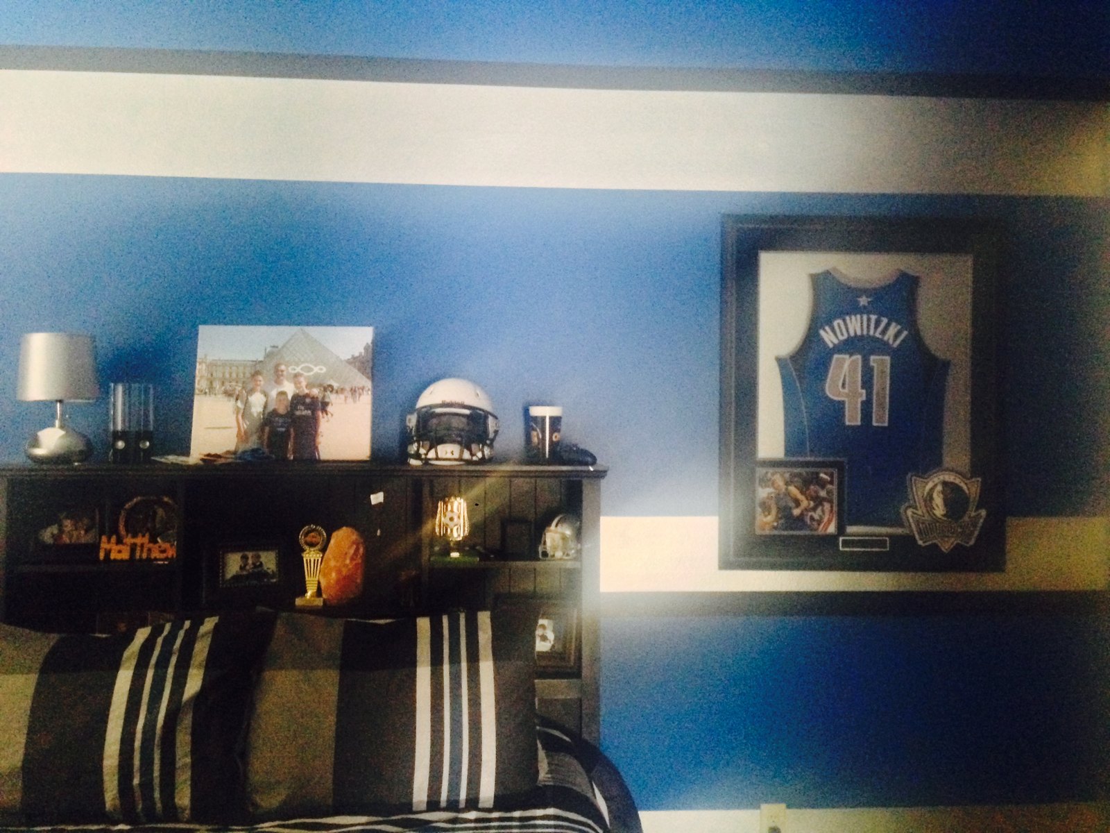 Bedroom with a blue and white striped wall, bookcase headboard and framed jersey