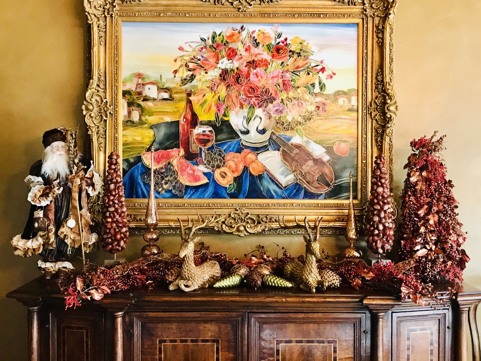 Console beneath a large still-life painting, flanked by fruited garlands and a Santa figure