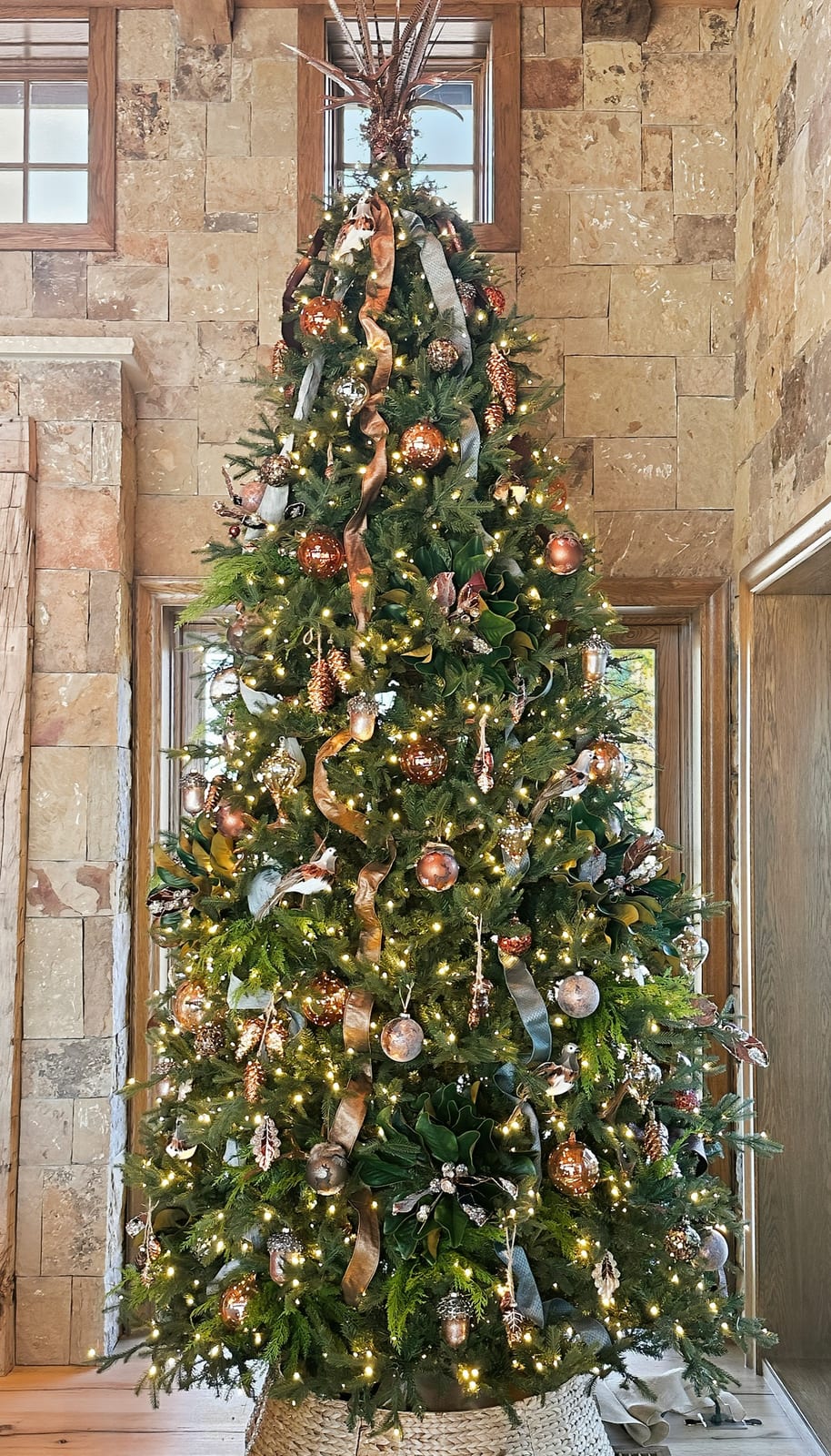 Tall Christmas tree in copper and gold against a stone wall in a double-height room