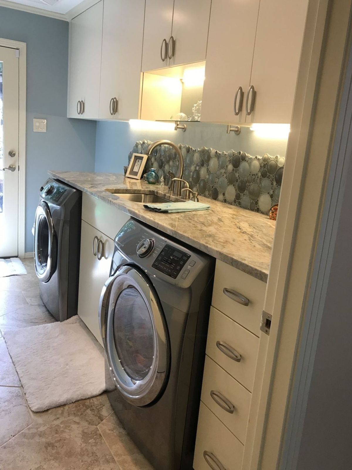 Built-in laundry room with custom cabinetry, stone counter and glass mosaic backsplash, built by Chateau Concepts in Dallas