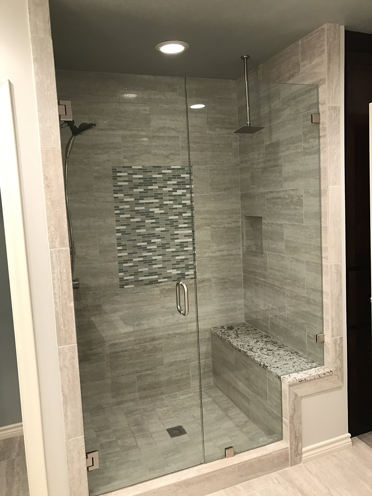 Newly built walk-in shower with a mosaic tile band, bench and frameless glass