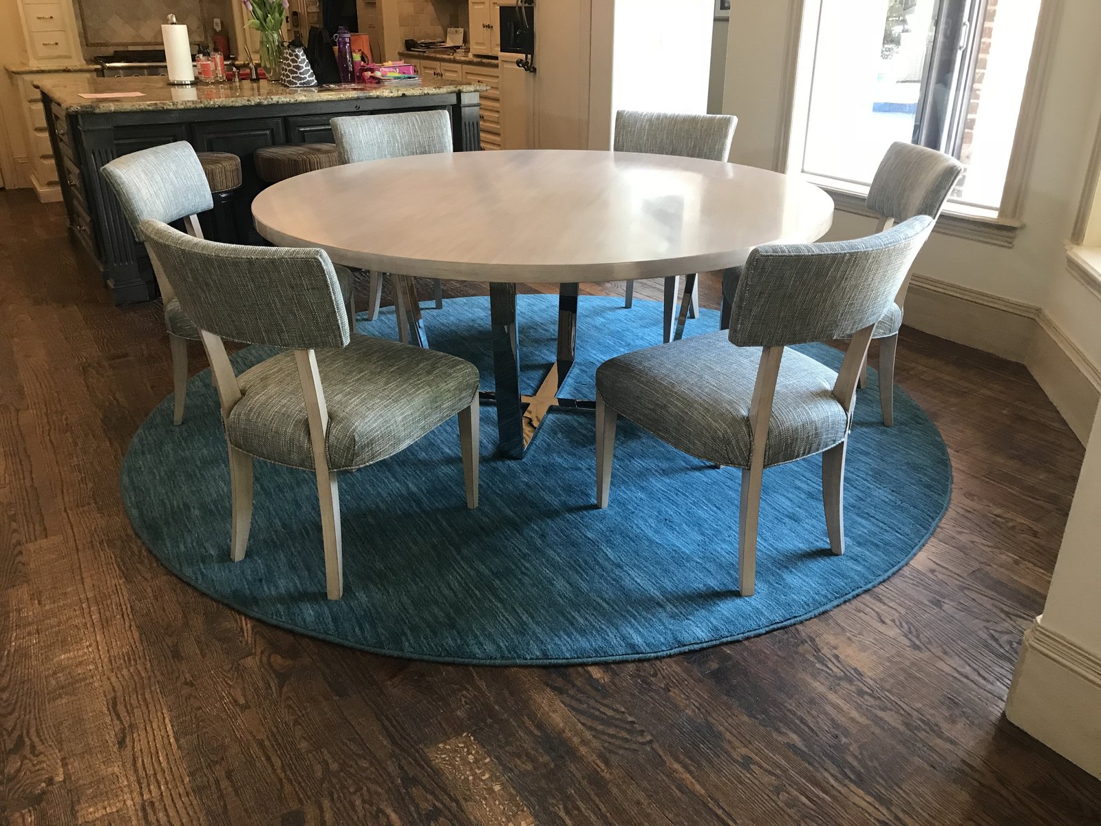 Round breakfast table with woven chairs on a teal round rug